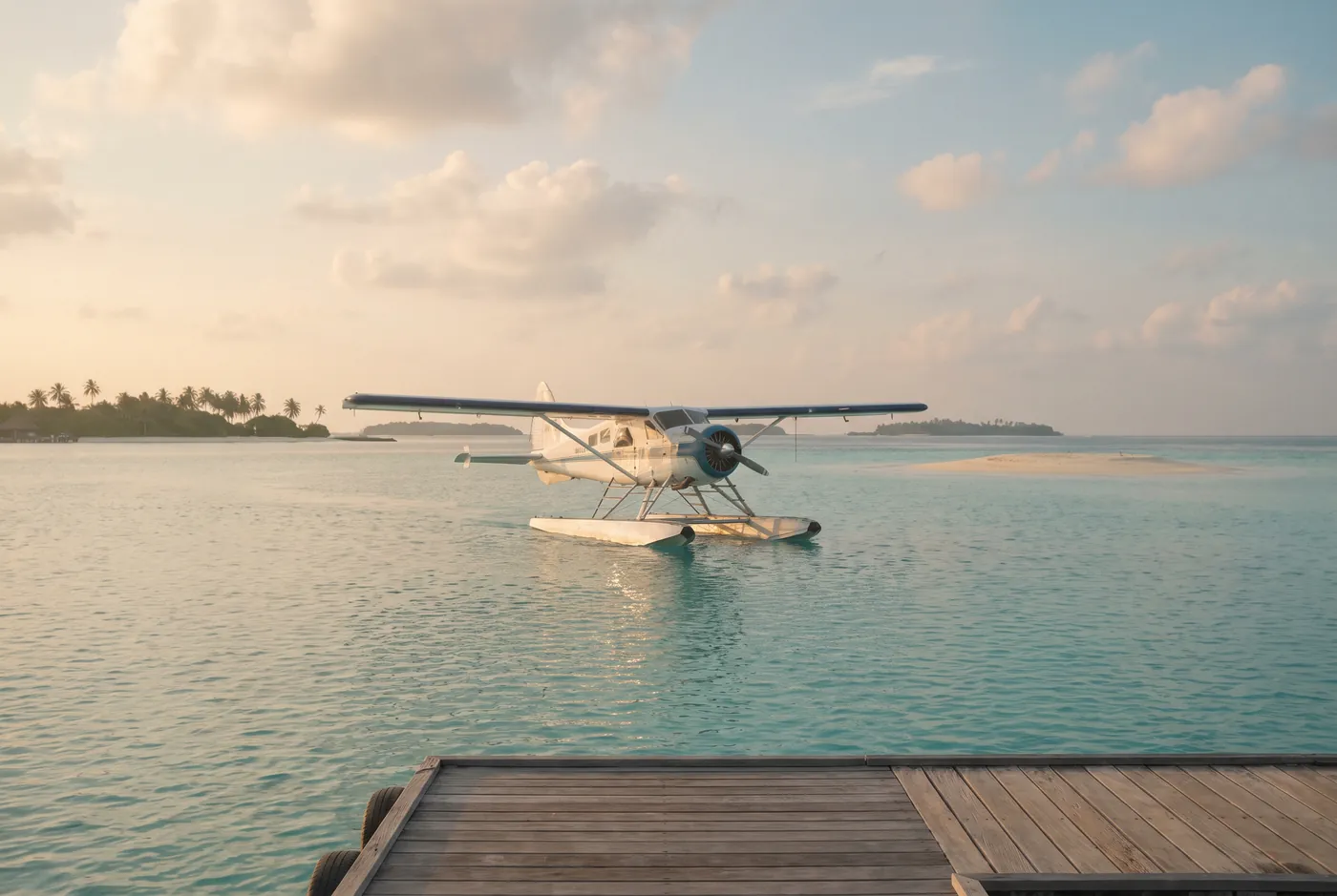 A seaplane resting on a calm turquoise Maldives lagoon at soft golden light